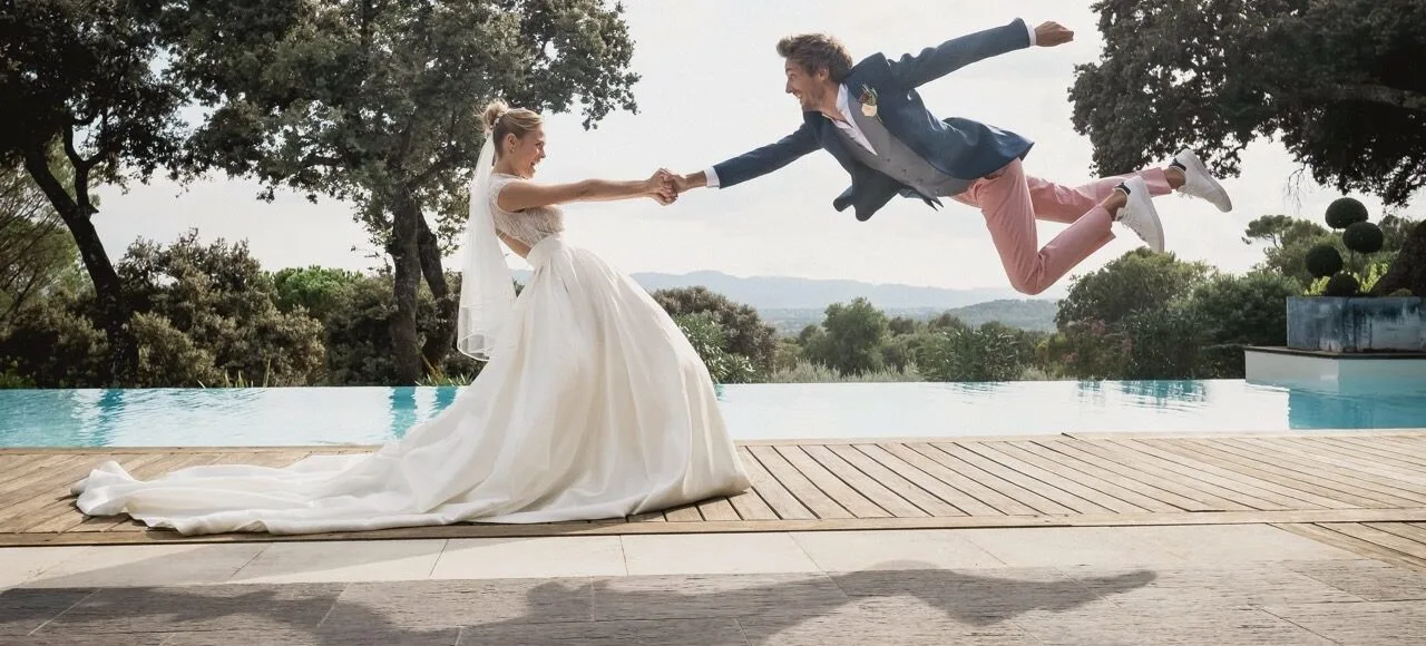 Marié sautant vers sa femme au bord d'une piscine, photo de mariage joyeuse et non posée