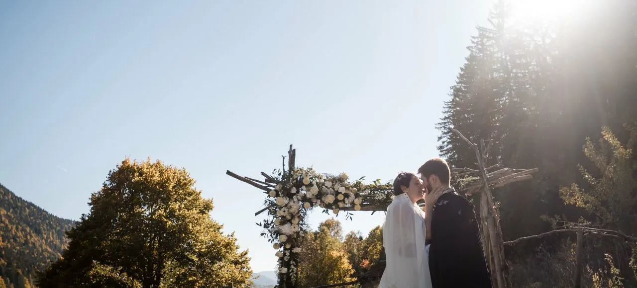 Cérémonie laïque sous une arche fleurie en contre-jour, mariage en plein air