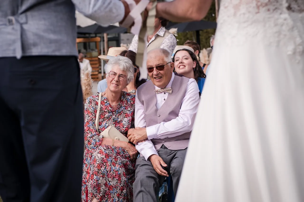 Grands-parents émus assis pendant la cérémonie, robe de la mariée au premier plan