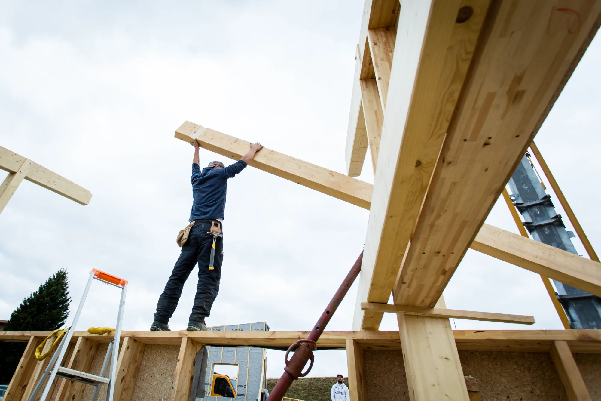 Charpentier debout sur une charpente en construction, contre-jour de chantier