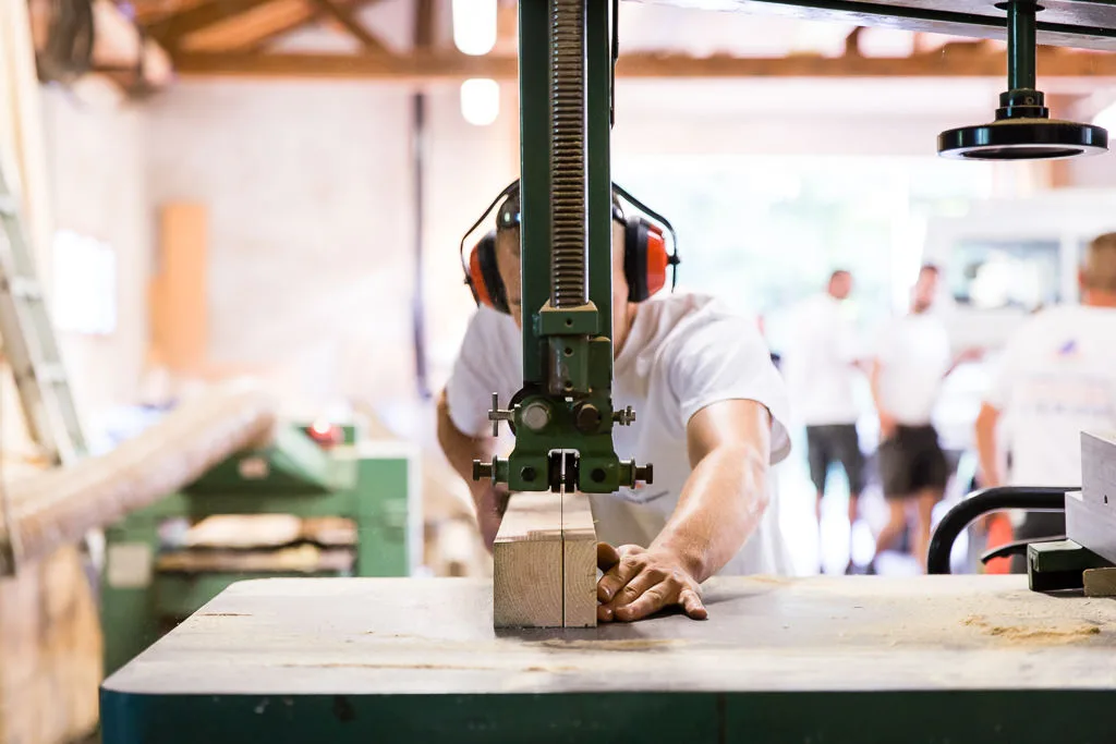 Menuisier découpant une pièce de bois à la scie à ruban dans son atelier